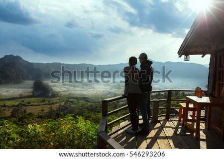 Silhouette couple looking at the beautiful sunrise on the top of mountain with the view into misty