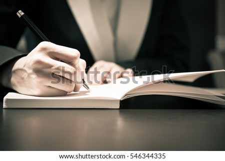 Close up of business people hand in suit writing on notebook or document
