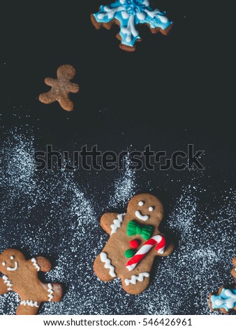 Christmas gingerbread men cookies. Variety of merry human-shaped ginger cookies with stripped lollipops on a black background dusted with sugar powder