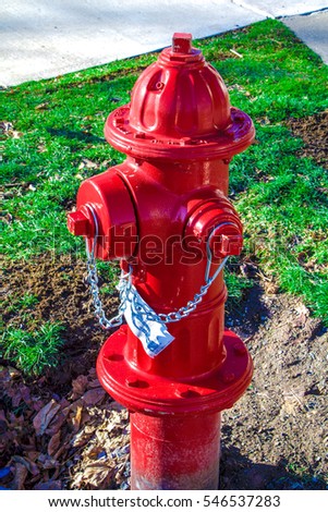Up close winter exterior daytime picture of red metal fire hydrant with green grass and cement sidewalk in the background.