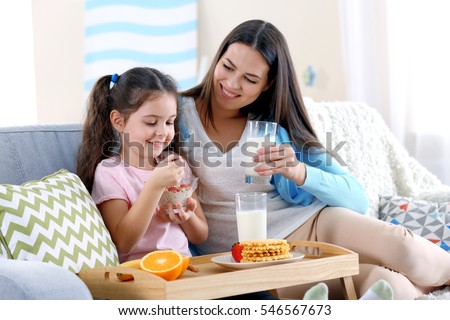Mother and daughter having healthy breakfast on sofa in room Royalty-Free Stock Photo #546567673