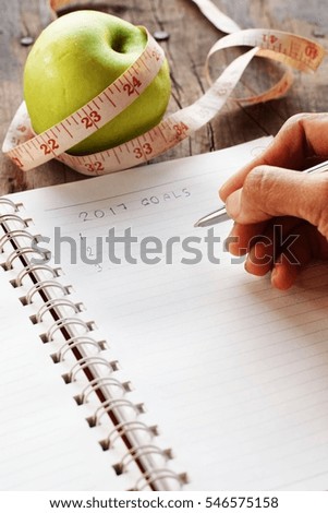 Diet plan concept,Green apple with measuring tape and a hand writing on a book