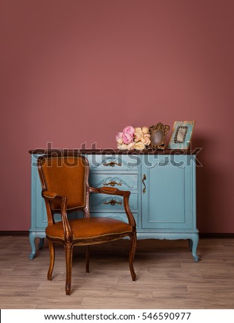 Retro brown leather armchair near blue dresser, tender bouquet and two frames. Blue and brown vintage interior. Brown room with ethnic dresser and chair. Antique cupboard. Clothes closet. Vanity Table Royalty-Free Stock Photo #546590977