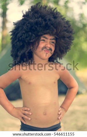 Little laughing boy in a black caucasian fur hat with painted mustache, eyebrows and beard