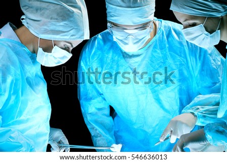 Medical team performing operation. Group of surgeon at work in operating theatre toned in blue.