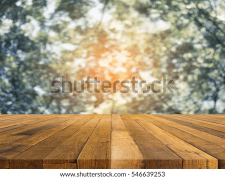 wood table and blur image of Abstract Bokeh of green tree with sun for background usage.