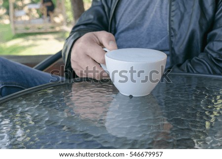 Man holding hot cup of coffee with more milk foam on the glass table. Loving coffee concept.