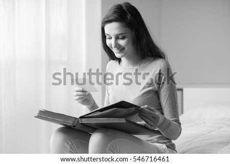 Young serene woman sitting on the bed at home and watching old pictures on a photo album