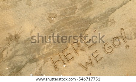 Handwriting words "HERE WE GO!" on sand of beach