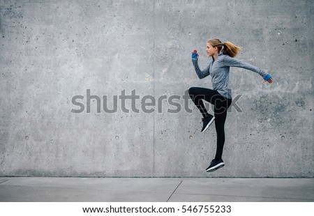 Side view shot of fit young woman doing cardio interval training against grey background. Fitness female exercising outdoors in morning. Royalty-Free Stock Photo #546755233