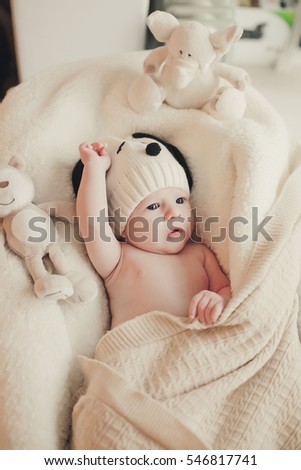 The baby lies wrapped in a knitted blanket. Smiles. Child knit beanie. Newborn smiling mother and surprised. On a white background