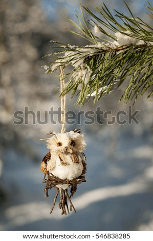 Handmade toy owl hanging on a pine branch in the snowy forest