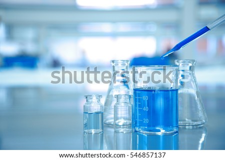 blue drop into glass beaker with flask and science laboratory background  Royalty-Free Stock Photo #546857137