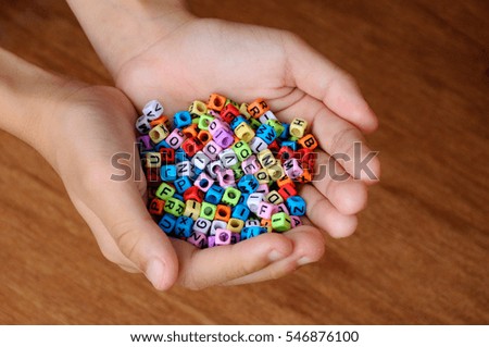 Children hand holding colorful small plastic cube with alphabet printed on it.