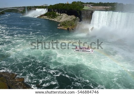 Landscape shot of both American and Canadian falls at Niagara Falls with the boat in front and rainbow across the bottom of the photo