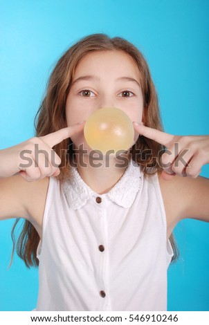 Girl blowing a big bubble gum bubble isolated on blue