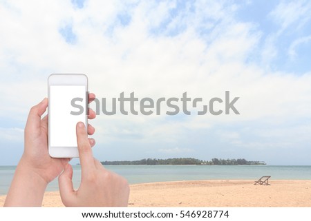 Female hand holding a phone on blur old beach wooden chairs on tropical beach