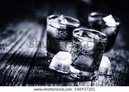 Black and white photo. Alcoholic cocktail from cola with whiskey and ice cubes,  wooden background, selective focus
