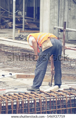 Reinforcing ironworker working on concrete formwork at construction site. Vintage style.