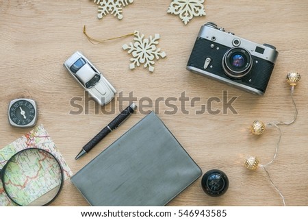 Vintage Photo Camera, Note Book, Compass, Pen, Magnifying Glass, Car, Christmas garland, Snowflakes , Map on The Wooden Background