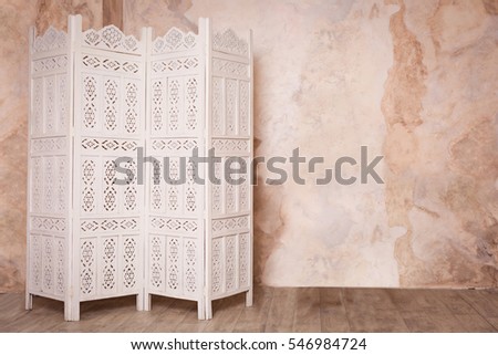 White delicate decorative wood panel on brown plaster wall. Boudoir wedding room. Retro folding screen. Vintage ornate carved folding screen.  Royalty-Free Stock Photo #546984724