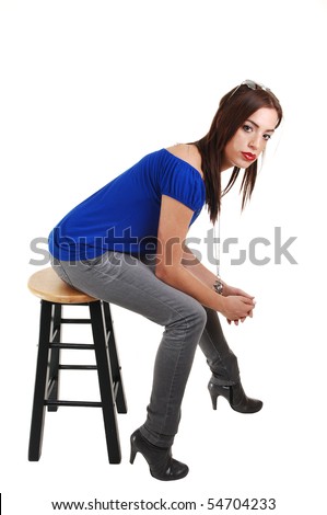 A young pretty woman, in a blue t-shirt, gray jeans and black boots sitting on a green bar chair, for white background.