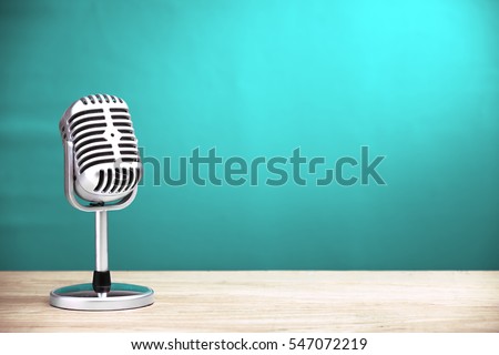 Retro microphone on wooden table with turquoise wall background Royalty-Free Stock Photo #547072219