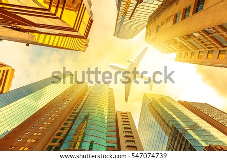 Airplane flying over modern skyscrapers on Hong Kong, Central District with sun light of sunset sky. Glass high-rise facade. Concept of transport, travel and business. View from bottom skyscrapers.