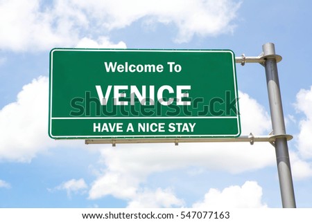 Green overhead road sign with a Welcome to Venice, Have a Nice Stay concept against a partly cloudy sky background.