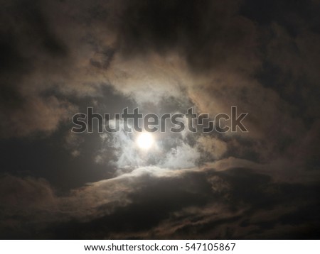 Sun Among Dark Clouds - Photograph of an afternoon sun surrounded by dark clouds, with some iridescence showing. Selective focus on clouds.  