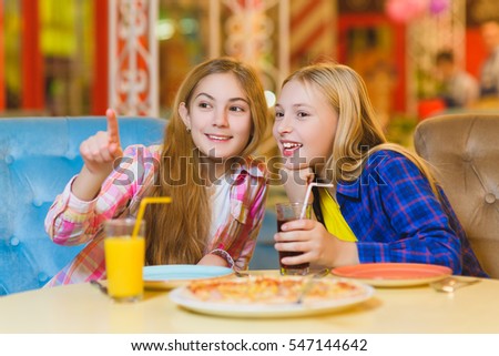 Two smiling girls eating pizza and drinking juice indoor
