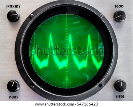 Very old oscilloscope. Round face is green plastic film that is not even, somewhat dirty. Fuzzy trace on display shows peaks. Controls in each corner.  Focus on grid in center. Royalty-Free Stock Photo #547186420