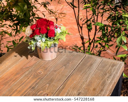 rose artificial flowers in the pot , on the wood desk, in the garden