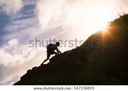 Young man climbing up a mountain. Self improvement and life goals concept.  Royalty-Free Stock Photo #547238893