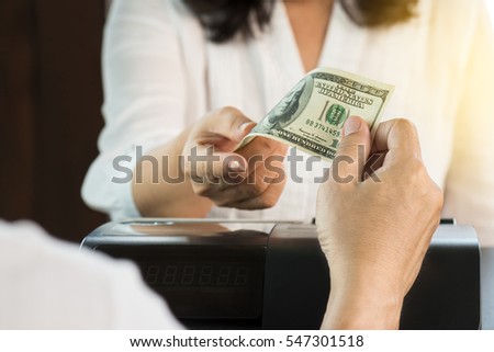  
Male customer paying 100 dollar bill  to a woman cashier at register counter .Pay with cash at retail shop.