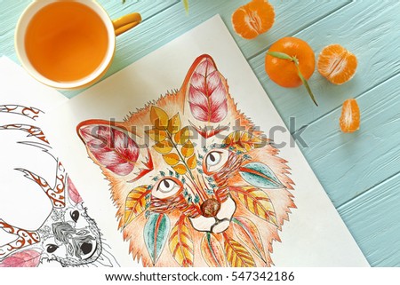 Colouring pictures, cup of tea and mandarins on wooden table, closeup