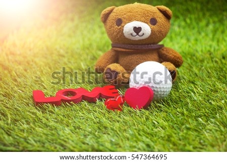 Golf ball and red heart shape are on the green grass. Sign of golfer in love.