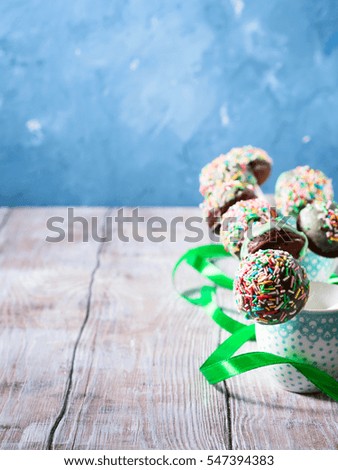 Closeup of colorful chocolate cake pops with sugar sprinkles in small coffee cups on wooden table. Copy space. Vertical