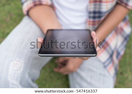 Young man or male hipster in casual wear sitting on green field  relax looking at blank screen digital tablet, close up.