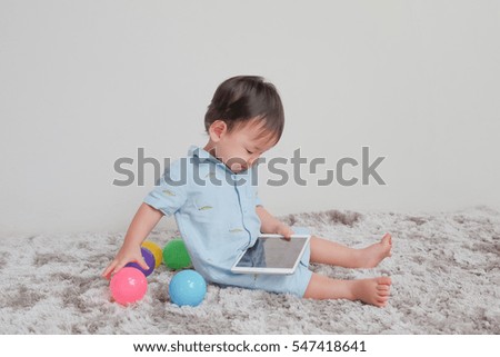 Adorable toddler boy sitting on the carpet and playing tablet and colorful toy on a floor