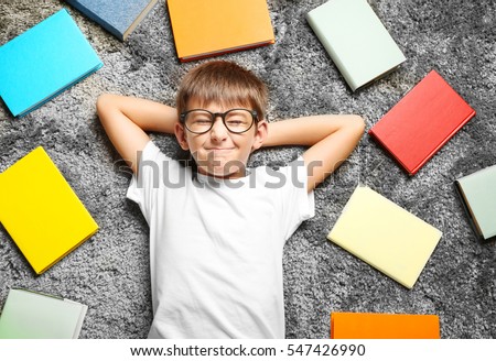 Cute schoolboy lying among books on carpet, top view Royalty-Free Stock Photo #547426990