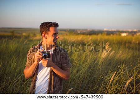 Handsome young traveler man with vintage camera,on a green meadow background. Travel mood. Photography. Relaxation on a field and sunset. Explore nature.