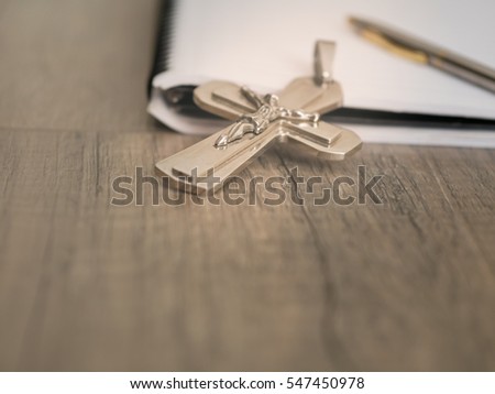 The silver crucifix and a pen on the a blank note book over wooden background, christian concept