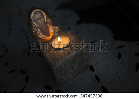 A wooden piece of wood with a picture of a holy figure illuminated by a small candle on  block of salt. The light is subtle and warm.