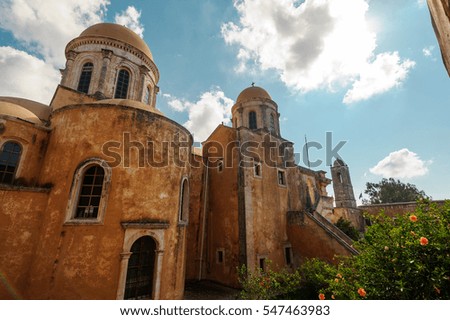 Picturesque shot of an ancient church with old walls, huge domes and interesting windows. Green plants, flowers, blue sky with the clouds as a nice decoration for such a nice landmark.