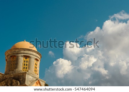 Big dome of an ancient church with the blue sky and huge white cloud in the background. Old landmark of a Greek culture and architecture.