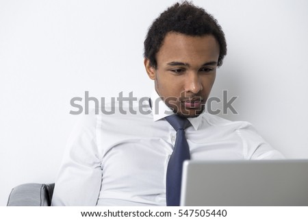 Close up of an African American businessman sitting in a leather armchair with his laptop. He is looking attentively at the screen.