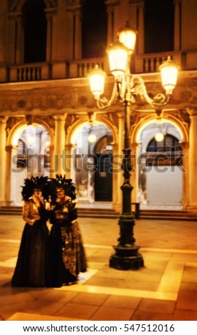 Blurry image of two mysterious female masks at San Marco square at night during the Carnival. Venice (Italy)