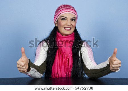 Beautiful woman in winter clothes sitting at table and giving thumbs up with both hands over blue background