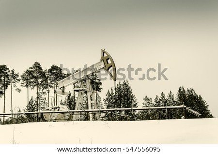 Pump jack and wellhead in the oilfield situated in the beautiful winter forest. Environmental pollution. Oil and gas concept. 